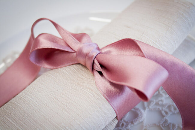 Dettaglio di un tovagliolo color avana legato da un nastro di raso rosa.